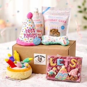 May include: A dog birthday gift box containing a party hat, bone-shaped toy, treats, and a plush cake. The party hat says "Let's Pawty" and the box has the "Bark Boxes" logo.