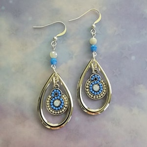 Puede incluir: Un par de pendientes de plata con cuentas azules y blancas. Los pendientes tienen forma de lágrima con un círculo más pequeño en el interior.