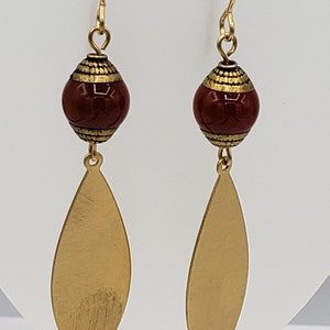 May include: A pair of gold tone dangle earrings with a red gemstone bead and a leaf-shaped pendant.