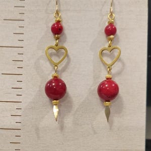 Op de afbeelding: Gouden oorbellen met rode kralen en open hartcharms. De oorbellen hebben een gouden haaksluiting.