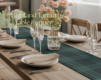 May include: A table setting with a Highland Tartan table runner. The runner is dark green with a plaid pattern in teal and pink. The table is set with plates, silverware, and champagne flutes. A vase of pink flowers sits in the center.
