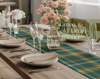 May include: A dining table set for a meal, featuring a green and gold tartan runner. The table is set with white plates, silverware, and champagne flutes. A vase of pink flowers adds a touch of color to the scene.