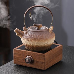Könnte beinhalten: Eine braune Keramik-Teekanne mit gebogenem Griff und einem kleinen dekorativen Anhänger. Die Teekanne steht auf einem Holzsockel mit einem Bedienknopf. Dampf steigt aus der Teekanne auf, was darauf hindeutet, dass sie in Gebrauch ist.