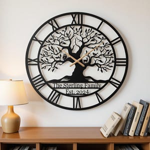 May include: A large circular black wall clock featuring a detailed tree silhouette with an owl, a deer, and a bird. The clock face displays Roman numerals and the text The Sterling Family Est. 2024. It has two thin light-colored wooden clock hands.