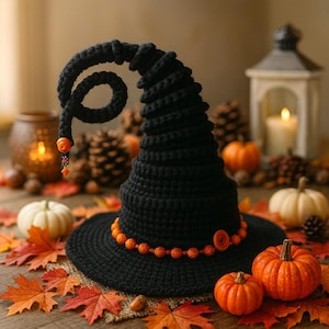Könnte beinhalten: Ein schwarzer Häkel-Hexenhut mit orangefarbenem Perlenbesatz und Knopf. Der Hut ist von Kürbissen, Herbstblättern und einer brennenden Kerze umgeben, was eine festliche Halloween-Szene schafft. Die spiralförmige Spitze des Hutes verleiht eine skurrile Note.