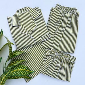 May include: Olive green and white striped pajama set. The set includes a button-down shirt with white trim and matching elastic-waist pants. The fabric has a vertical stripe pattern. The pajamas are neatly arranged on a white surface.