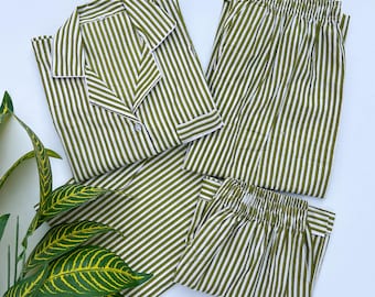 Op de afbeelding: Olijfgroene en wit gestreepte pyjamaset. De set bevat een overhemd met knopen en witte rand en een bijpassende broek met elastische tailleband. De stof heeft een verticaal streepjespatroon. De pyjama's zijn netjes op een wit oppervlak geplaatst.