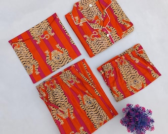 Op de afbeelding: Een set oranje en roze gestreepte pyjama's met een tijgerprint. De set bevat een overhemd met knopen, een broek en een korte broek. De pyjama's zijn netjes op een wit oppervlak gevouwen. Een klein paars en blauw bloemstuk staat in de hoek.