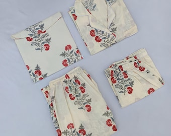 Op de afbeelding: Crèmekleurige pyjamaset met een bloemenpatroon van rode bloemen en groene bladeren. De set bevat een top met lange mouwen en kraag, een broek en een bijpassende tas. De pyjama is netjes op een lichtgrijze ondergrond gevouwen.