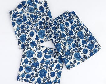 May include: A blue floral pajama set, including a button-down shirt, shorts, and a sleep mask. The set features a white background with a repeating pattern of blue flowers and foliage. The shirt has white piping.