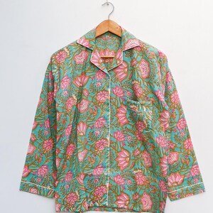 Op de afbeelding: Een pyjamajas met lange mouwen en een bloemenpatroon in teal, roze en groen. De top heeft een kraag, een borstzak en witte biezen. Het kledingstuk hangt aan een houten hanger tegen een witte achtergrond.