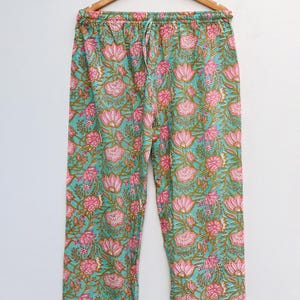 Op de afbeelding: Pyjamabroek met bloemenprint in teal, roze en bruin. De broek heeft een taille met trekkoord en een witte bies aan de onderkant. Het bloemenpatroon bevat grote roze bloemen en kleinere bloemaccenten.