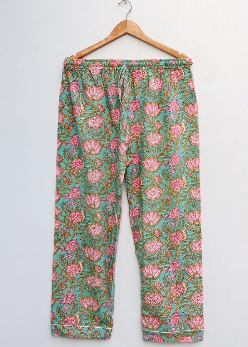 Op de afbeelding: Pyjamabroek met bloemenprint in teal, roze en bruin. De broek heeft een taille met trekkoord en een witte bies aan de onderkant. Het bloemenpatroon bevat grote roze bloemen en kleinere bloemaccenten.