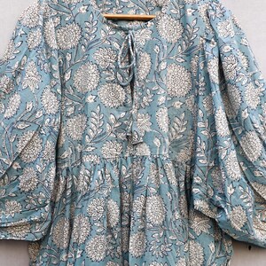 May include: A light blue dress with a white floral pattern. The dress has long sleeves, a round neckline with a tie, and a tiered skirt. The fabric appears to be lightweight and suitable for warm weather.