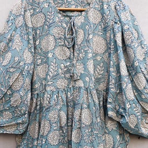 May include: A light blue dress with a white floral pattern. The dress has long sleeves, a round neckline with a tie, and a tiered skirt. The fabric appears to be lightweight and suitable for warm weather.