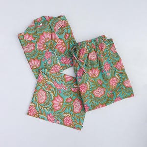 Op de afbeelding: Een bijpassende pyjamaset met een turquoise bloemenpatroon met roze en groene accenten. De set bevat een overhemd met knopen, een korte broek en een bijpassende trekkoordtas. De pyjama is gemaakt van een zachte, lichte stof.