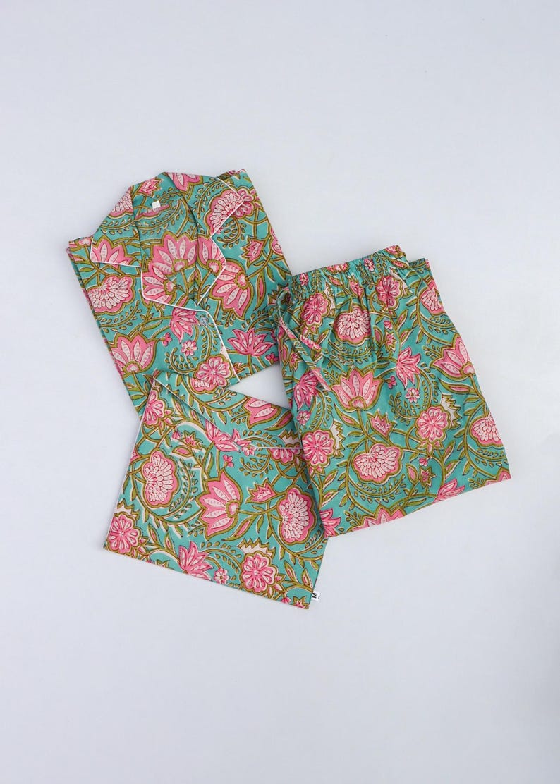 Op de afbeelding: Een bijpassende pyjamaset met een turquoise bloemenpatroon met roze en groene accenten. De set bevat een overhemd met knopen, een korte broek en een bijpassende trekkoordtas. De pyjama is gemaakt van een zachte, lichte stof.
