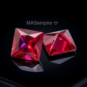 Op de afbeelding: Twee vierkant geslepen, levendig rode edelstenen met gefacetteerde oppervlakken die licht reflecteren. De tekst "MASempire" gevolgd door een klein diamanticoon staat boven de stenen tegen een donkere, reflecterende zwarte achtergrond.