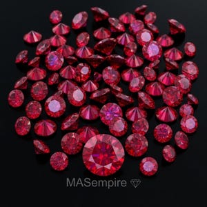 May include: A collection of numerous round-cut, vibrant red gemstones arranged in a cluster. The stones exhibit multiple facets that reflect light, creating a brilliant appearance. The text "MASempire" with a diamond icon is printed below.