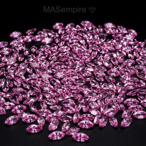 May include: A large collection of loose, faceted pink gemstones in a marquise cut, scattered across a solid black surface. The text MASempire with a small diamond icon is visible at the top center of the image, printed in a light gray color.
