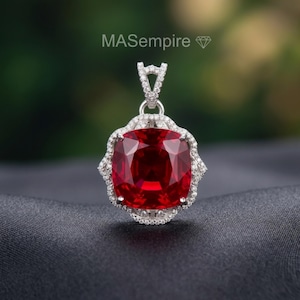 May include: A silver pendant with a large, square-cut, deep red gemstone at its center. The gemstone is surrounded by a halo of smaller, clear stones. The pendant has a decorative bail and is set against a dark background. The text "MASempire" is visible.