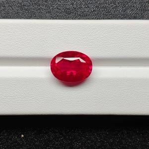 Peut inclure: Un rubis de forme ovale, d'un rouge vif et profond. Les facettes de la pierre précieuse captent et reflètent la lumière. Le rubis est posé sur un fond blanc, ce qui met en valeur son éclat. Gros plan sur la clarté et la couleur intense de la gemme.