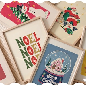 May include: A collection of framed art prints featuring holiday themes, including a snowman on a red background, Santa Claus, the text NOEL NOEL NOEL, a snow globe with a gingerbread house and the text Home for Christmas, and holiday cookies.