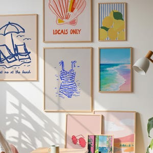 May include: A collection of framed art prints with a beach theme. The prints feature illustrations of a seashell, lemons, a swimsuit, beach chairs, and a coastal landscape. The color palette includes blues, pinks, and yellows, creating a summery vibe.