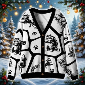 Könnte beinhalten: Ein weißer Cardigan mit schwarzem Besatz und Knopfverschluss. Der Pullover zeigt ein sich wiederholendes Muster aus schwarzen Waschbären mit Sonnenbrillen, Pfotenabdrücken und geometrischen Formen. Der Hintergrund ist eine Winterszene.