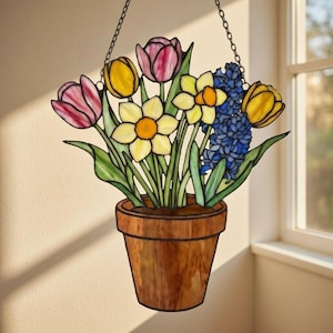 Könnte beinhalten: Buntglas-Blumenarrangement mit gelben Narzissen, rosa Tulpen und blauen Hyazinthen in einem braunen Topf. Die Glaskunst wird von einer Kette gehalten, geeignet für Fenster- oder Wanddekoration.