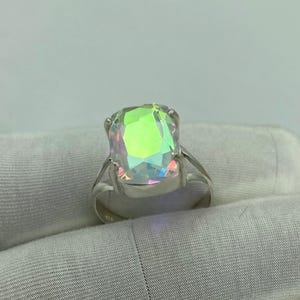 May include: A silver ring featuring a large, iridescent, rectangular gemstone. The gemstone displays a spectrum of colors, including green, yellow, and blue, reflecting light. The ring's band is a simple, polished silver design, showcasing the prominent stone.
