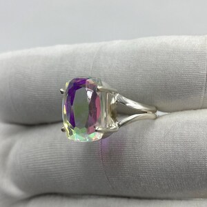 May include: A silver ring featuring a large, rectangular, iridescent gemstone. The gemstone displays a spectrum of colors, including purple, green, and pink. The ring's band splits into two parallel strands on each side of the stone.
