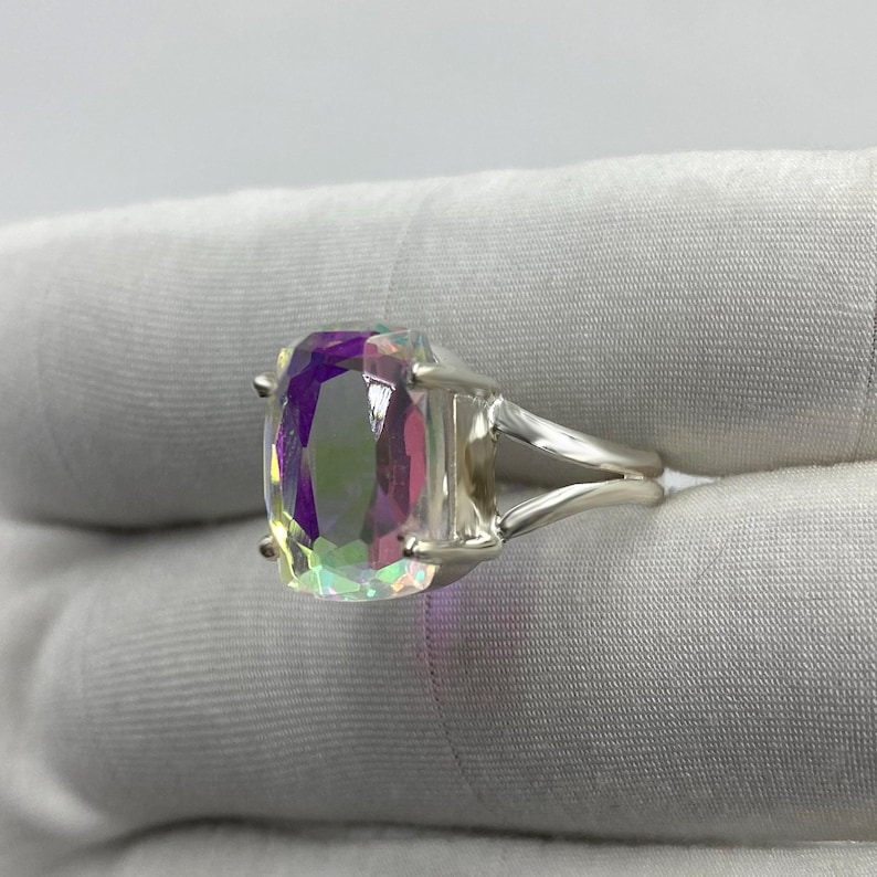 May include: A silver ring featuring a large, rectangular, iridescent gemstone. The gemstone displays a spectrum of colors, including purple, green, and pink. The ring's band splits into two parallel strands on each side of the stone.