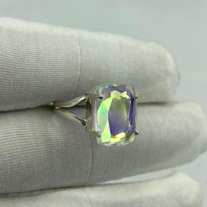 May include: A silver ring featuring a large, rectangular iridescent gemstone. The gemstone displays a spectrum of colors, including green, yellow, and purple, creating a shimmering effect. The ring's band has a split design, adding to its unique appearance.