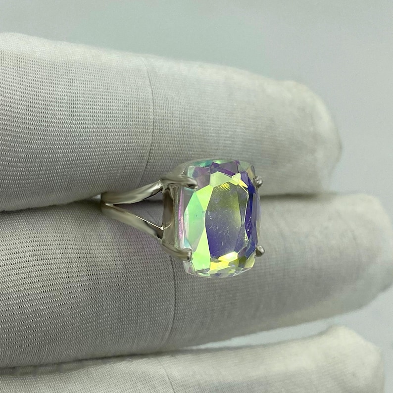 May include: A silver ring featuring a large, rectangular iridescent gemstone. The gemstone displays a spectrum of colors, including green, yellow, and purple, creating a shimmering effect. The ring's band has a split design, adding to its unique appearance.