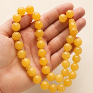 May include: A string of amber-coloured prayer beads, with smooth, round beads strung on a red cord. The beads are a warm, translucent yellow, and the design is simple and elegant.