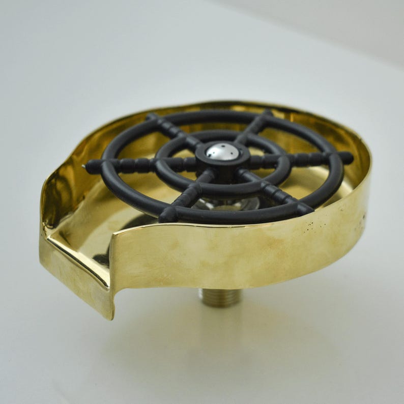 K&ouml;nnte beinhalten: Ein Sp&uuml;lbecken-Rinser aus Messing mit einem schwarzen, radf&ouml;rmigen Spr&uuml;her aus Kunststoff. Der Rinser hat ein kreisf&ouml;rmiges Becken und einen Gewindesockel zur Installation. Das Design ist einfach und funktional.