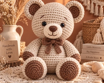 May include: A crocheted teddy bear in light beige with dark brown accents on the ears, paws, and a small bow tie. The bear has black eyes and a stitched nose. A wooden sign reads Handmade with Love, and books are titled Little Moments, Big Happiness, A Kinder World.