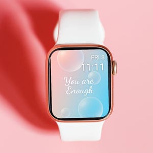 May include: A rose gold smartwatch with a white band displays the time as 11:11 on Friday. The screen features a gradient of blue and pink with the words "You are Enough" in white script. Bubbles float across the screen.