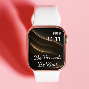 May include: A rose gold smartwatch with a white band displays the time as 11:11 on Friday, with the words "Be Present. Be Kind." on the screen. The watch is set against a soft pink background.