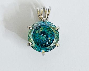 May include: A round, teal-colored gemstone pendant with a silver-colored setting. The gemstone has multiple facets, creating a sparkling effect. The pendant is suspended from a silver bail.