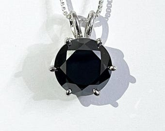 以下が含まれることがあります： 大きな黒いファセット宝石をあしらったシルバーペンダントネックレス。丸い宝石は6つの爪でセットされています。チェーンは繊細なシルバーリンクです。ペンダントは白い背景に表示されています。