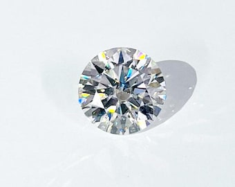 May include: A round, brilliant-cut diamond with multiple facets, reflecting light. The colorless gemstone is set against a white background, showcasing its clarity and sparkle. The diamond's shadow is visible.