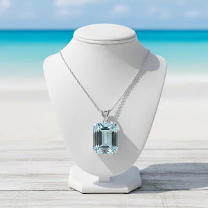 Puede incluir: Un collar de plata con un gran colgante de piedra preciosa azul claro, de corte esmeralda rectangular. La piedra transparente y facetada está engastada en un marco de metal sencillo y cuelga de una delicada cadena de plata.