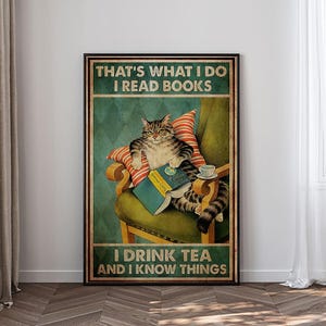 May include: A framed poster featuring a tabby cat seated in a green armchair, reading a book and drinking tea. The poster has the text "THAT'S WHAT I DO I READ BOOKS I DRINK TEA AND I KNOW THINGS."