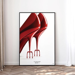 Puede incluir: Póster enmarcado con dos zapatos de tacón rojos brillantes con tacones en forma de tridente. El póster tiene un fondo blanco y un marco negro. El texto en la parte inferior dice "IN THEATERS MAY 1".