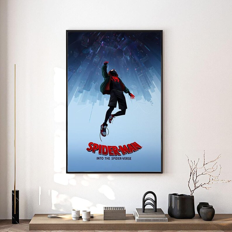 Może przedstawiać: Oprawiony plakat z postacią Spider-Mana z filmu "Spider-Man: Into the Spider-Verse". Grafika przedstawia Spider-Mana w powietrzu na tle panoramy miasta. Tytuł "Spider-Man Into the Spider-Verse" jest wyświetlany na czerwono.
