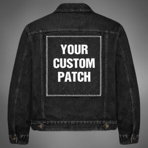 Może przedstawiać: Czarna kurtka dżinsowa z prostokątną białą naszywką z napisem "YOUR CUSTOM PATCH" wielkimi literami. Kurtka ma klasyczny krój z zapięciami na guziki i dwiema kieszeniami na piersi. Naszywka jest obrysowana białym zygzakowatym ściegiem.