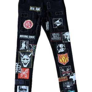 May include: Black denim jeans with various patches featuring text and graphics. Patches include the text "MISSING SINCE THURSDAY", "STAR TRAK", and "AKIRA". Other patches display images of a demon mask, a butterfly, and a shield.