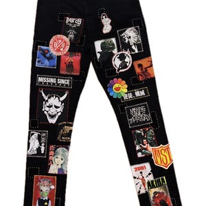 May include: Black denim jeans adorned with various patches featuring graphic designs, text, and illustrations. Patches include a smiling flower, a devil mask, and text that reads "MISSING SINCE THURSDAY".